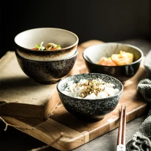 Trois bols en céramique japonais avec motifs variés, contenant divers plats, posés sur une planche en bois à côté de baguettes.