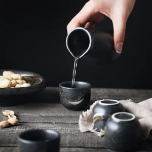 versement du saké dans un verre à saké japonais en céramique noir